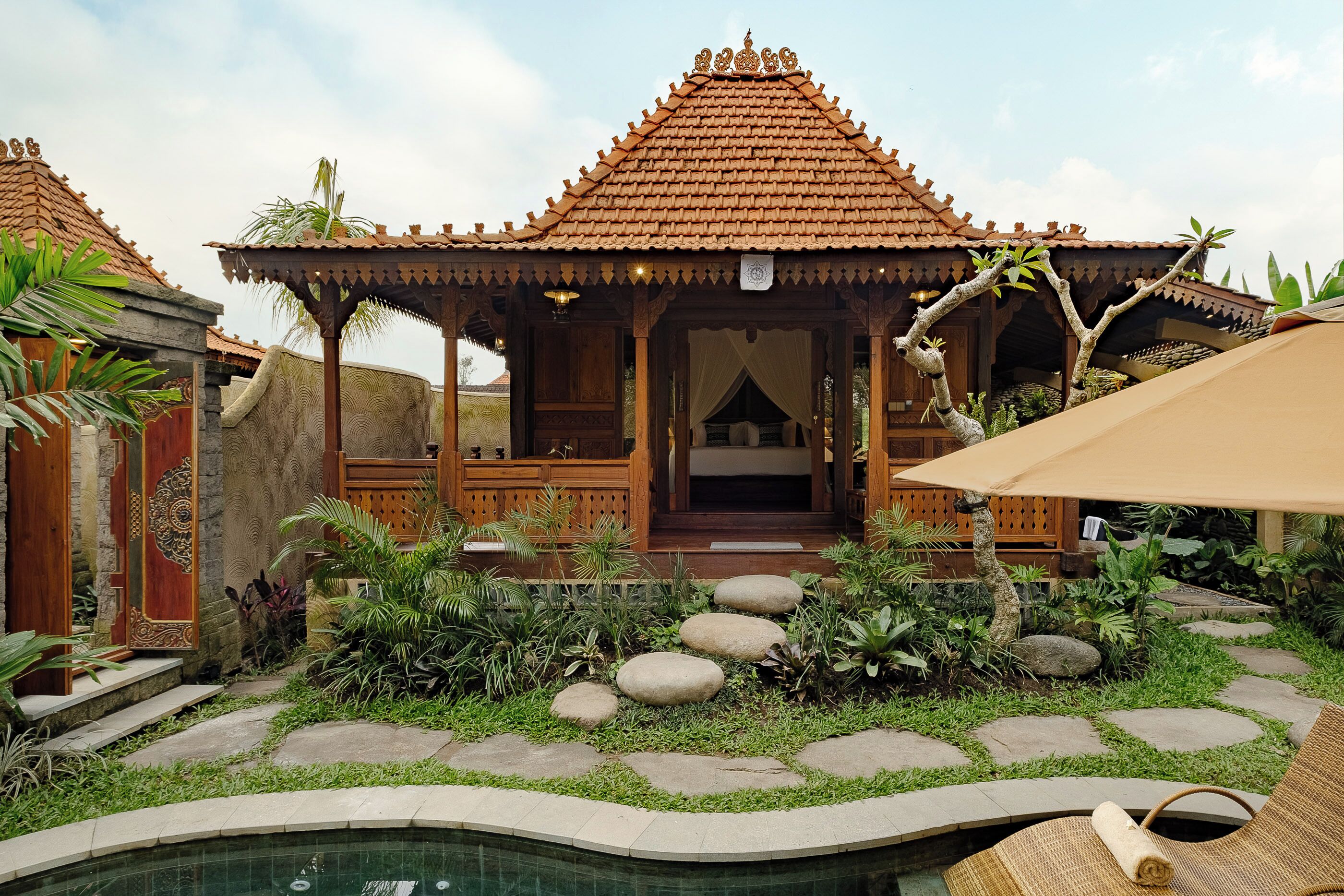 A traditional wooden structure with a tiled roof, a pool, and a garden with stepping stones and plants.