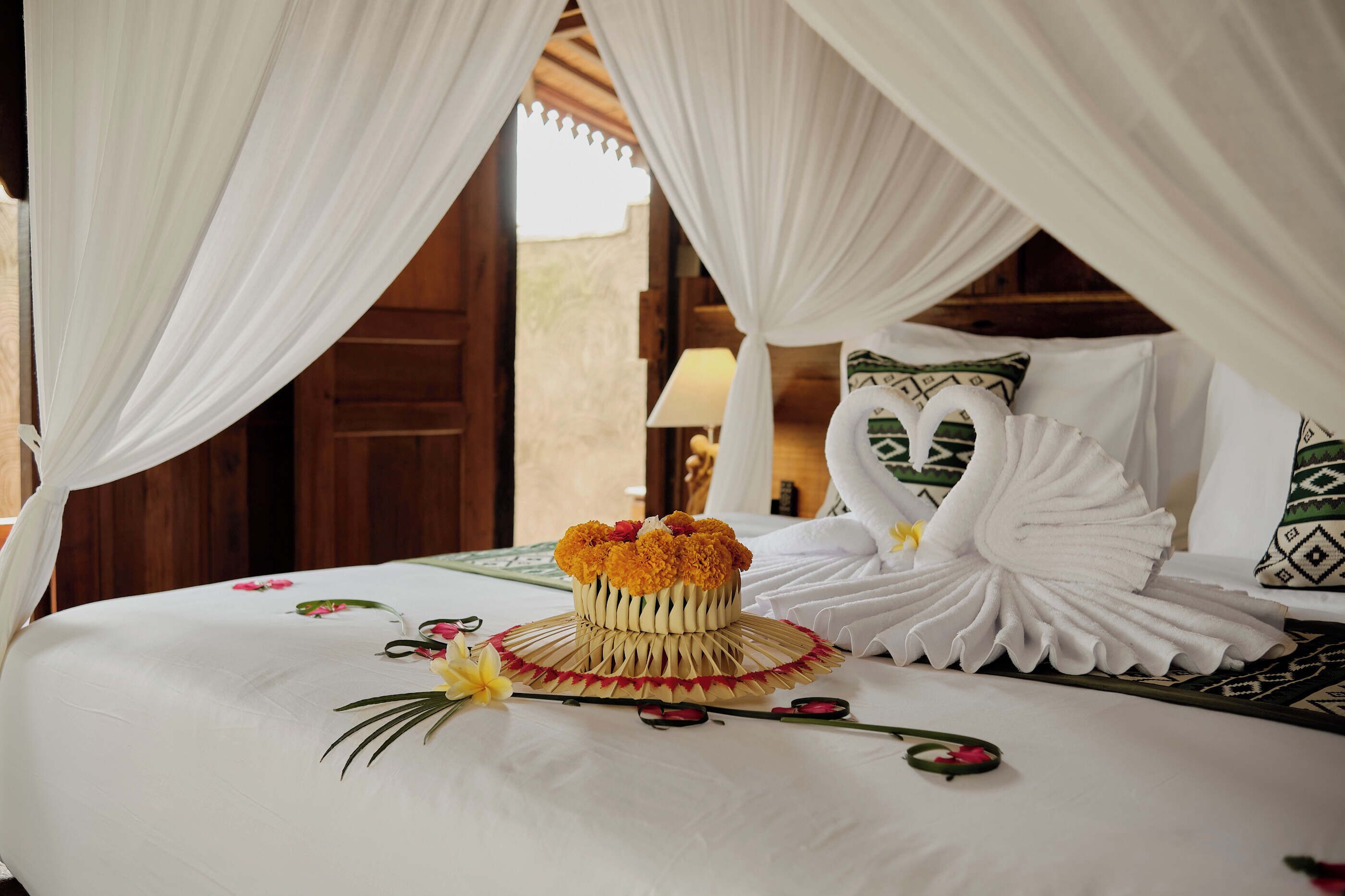 A bed with a decorative swan pillow, a woven basket with flowers, and a canopy.