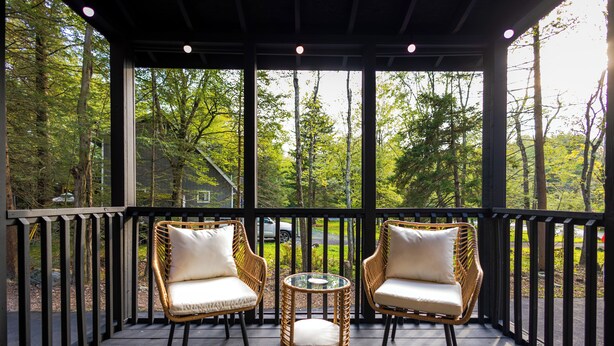 A covered outdoor seating area with wicker chairs and a glass table, surrounded by a wooden deck and a view of a forested area. - Deer Trails Retreat•Games•Fire Pit•Near Kalahari•Pocono•Camelback (Pocono Summit)