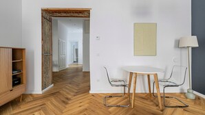 A modern room with a herringbone wooden floor, a round white table with two chairs, a wooden cabinet with shelves, and a lamp.
