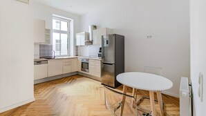 A modern kitchen with white cabinets, a stainless steel refrigerator, and a dining table with metal legs.
