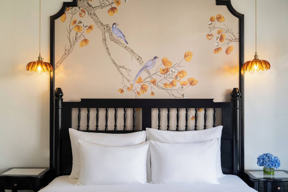 A bed with white linens, a black headboard with a painted tree branch and birds, and two bedside lamps.