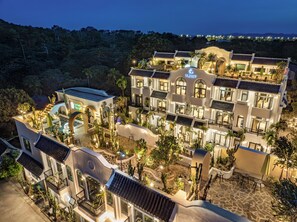 Een meerhoog hotel met een binnenterrein met cactussen en palmbomen, een zwembad en een restaurant genaamd "La Charm".