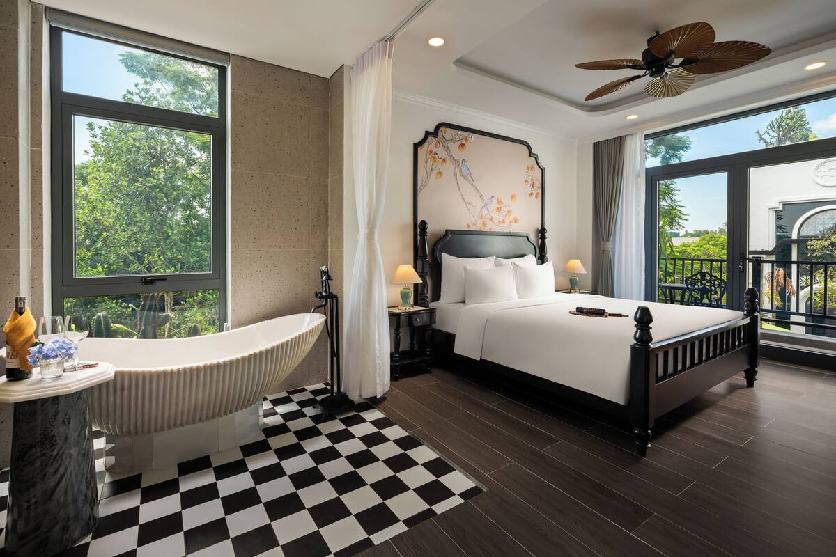 A modern bedroom with a large window, a bathtub, a bed, and a ceiling fan.