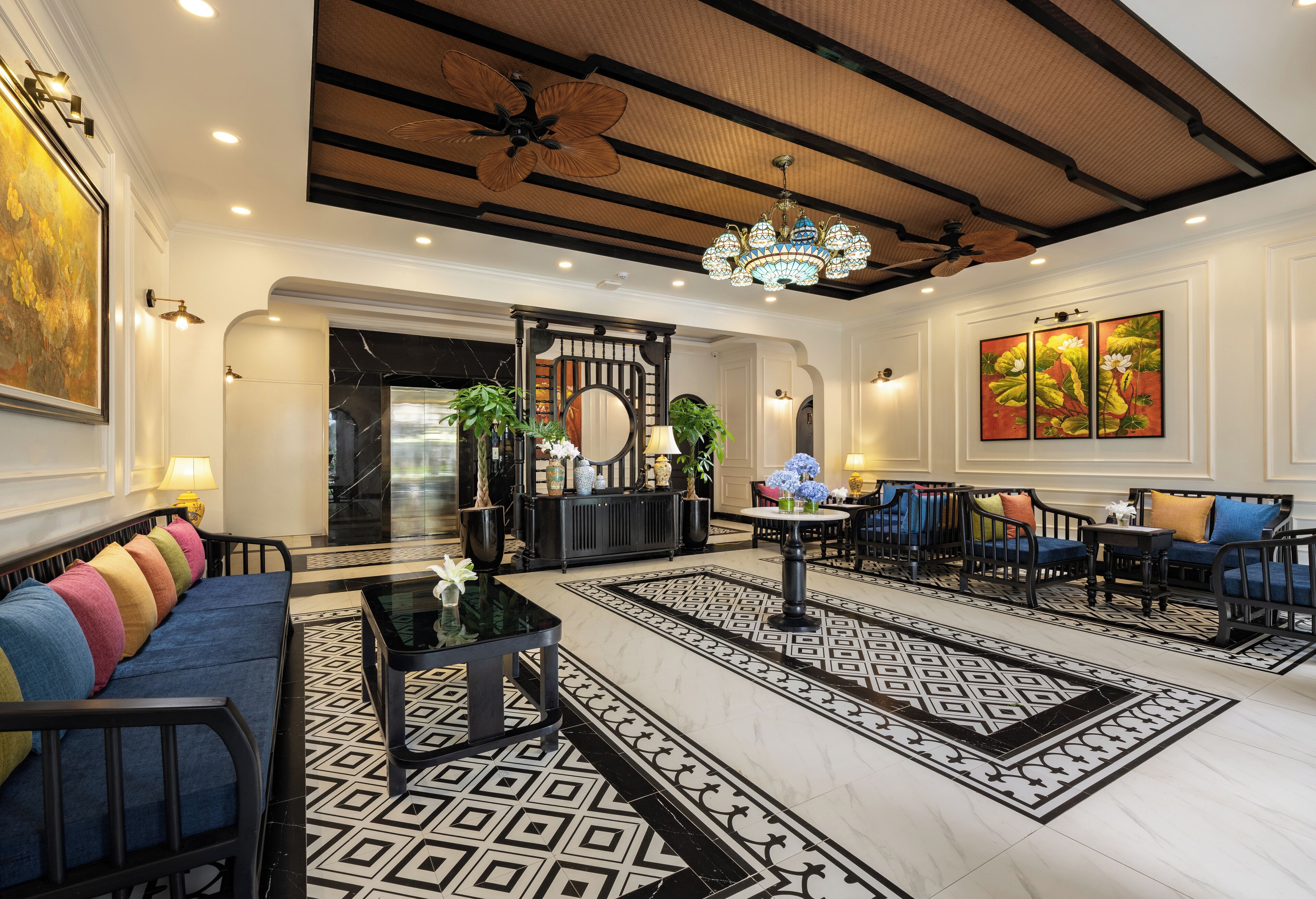 A spacious lobby with a black and white patterned floor, a blue sofa with colorful cushions, a black coffee table, and a chandelier.
