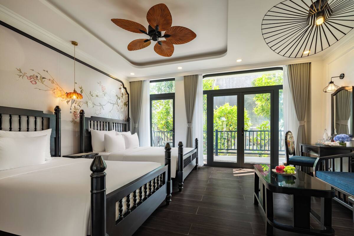 A hotel room with a large bed, a desk, and a balcony with a view of greenery.