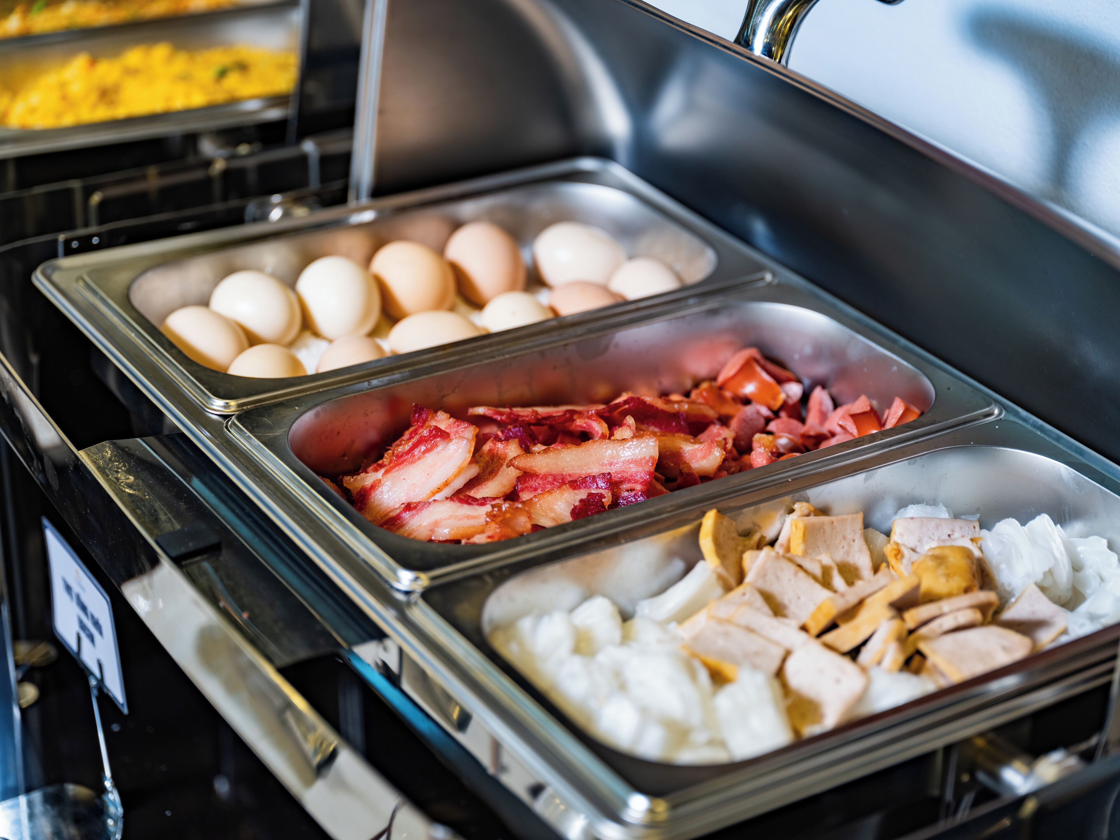 Un bufé con diversas opciones de comida, como huevos, tocino y pollo.
