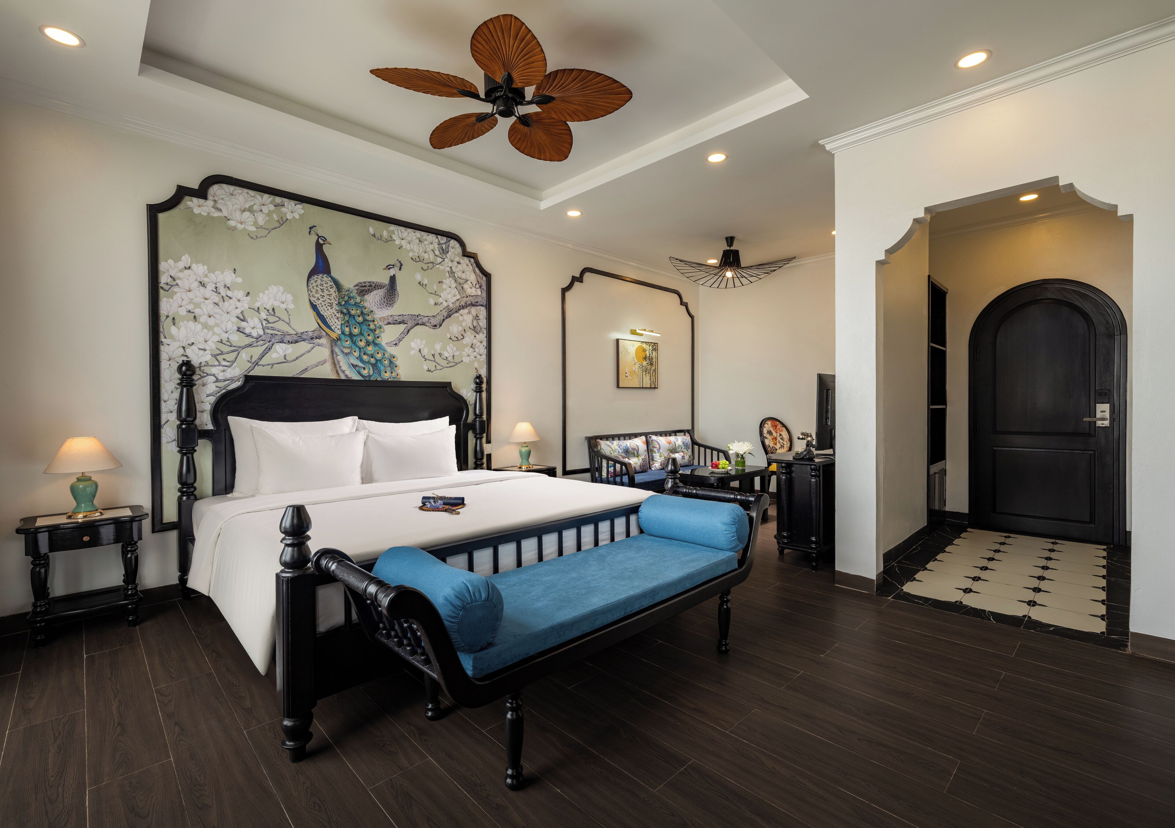 A bedroom with a large bed, a bench, a ceiling fan, and a door with a mat.