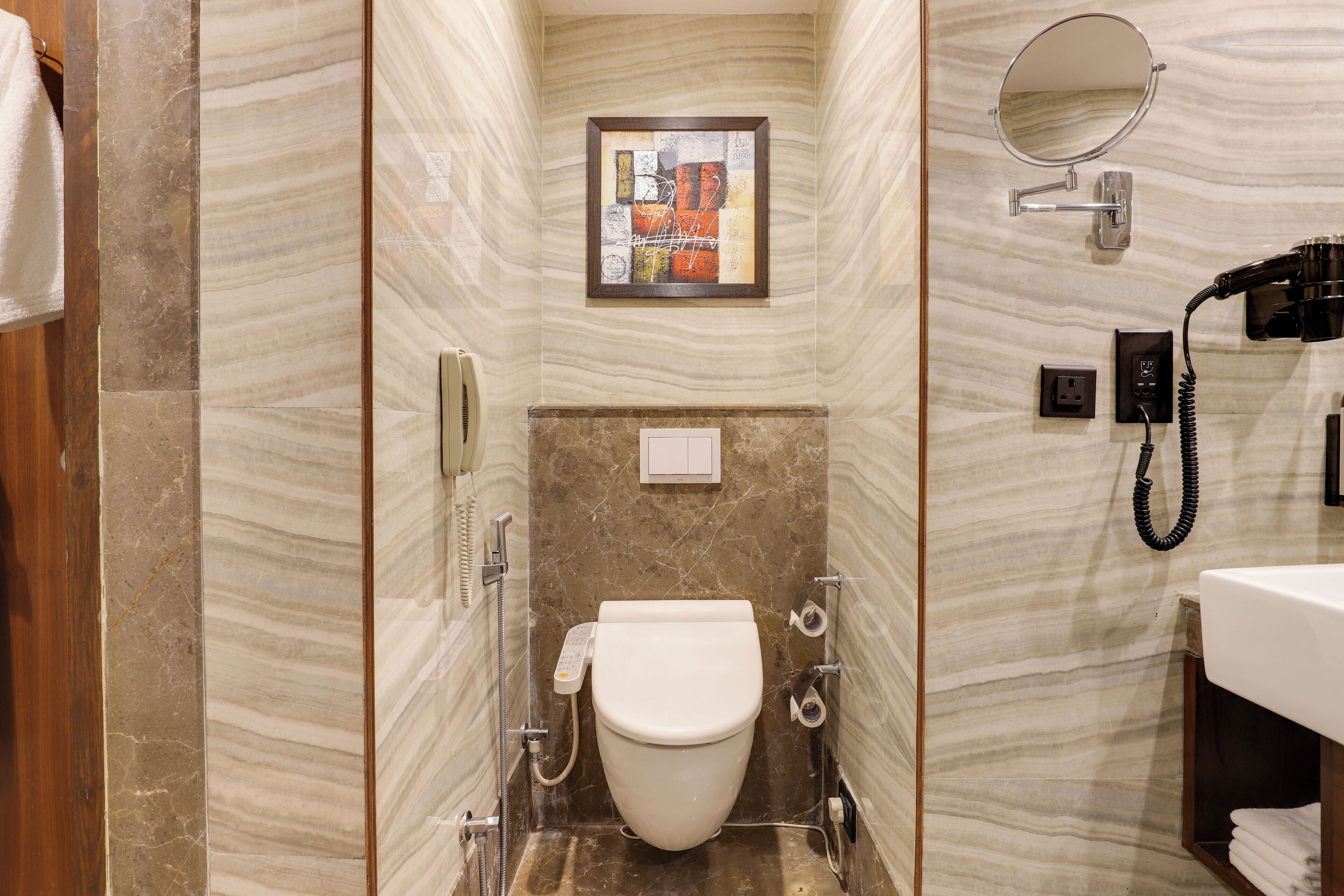 Un baño con inodoro, secamanos, toallero, espejo y teléfono.