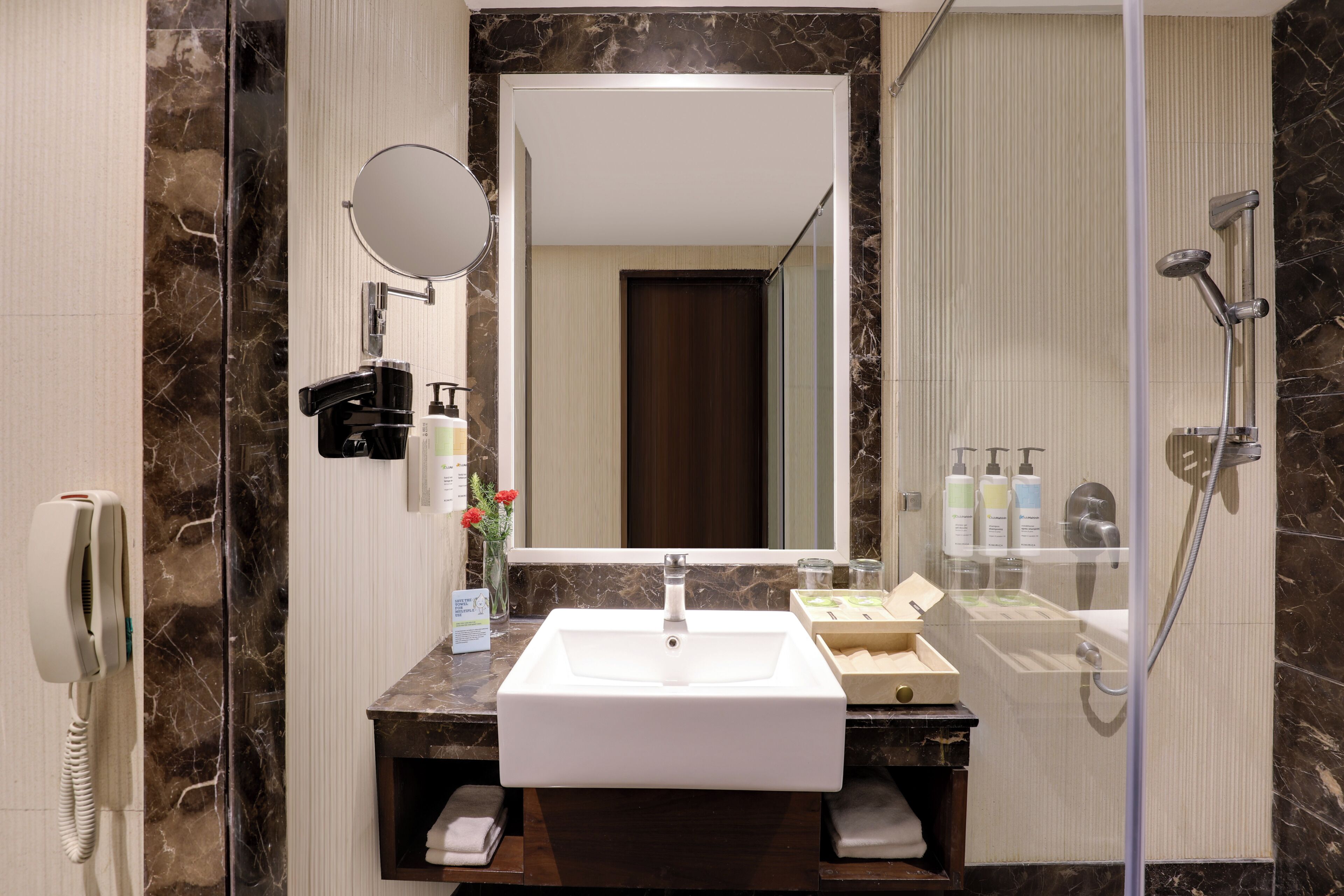 A modern bathroom with a marble sink, a mirror, a telephone, and a shower.