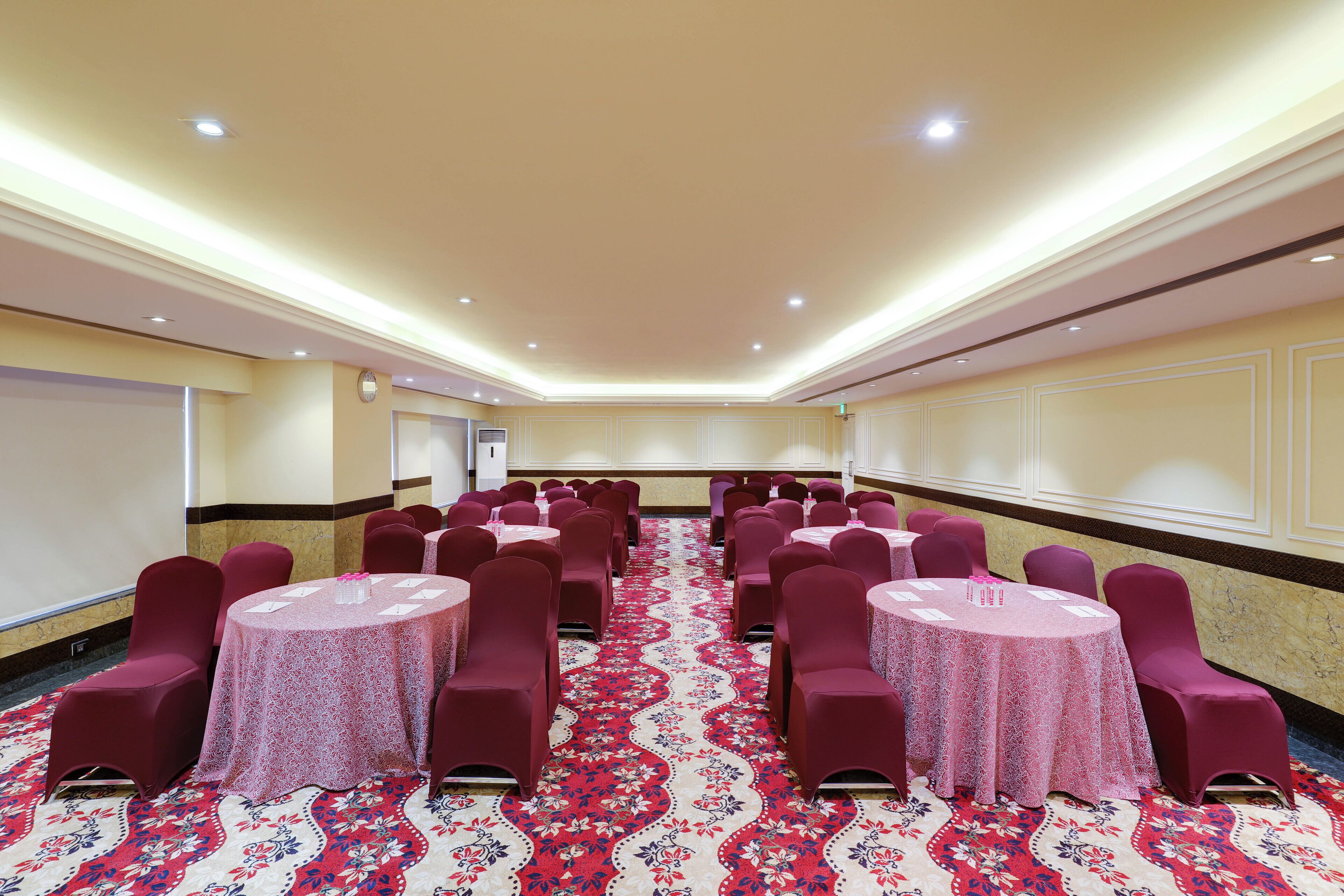 Une salle de conférence avec des tables et des chaises rondes, une moquette à motifs et un tableau blanc au mur.