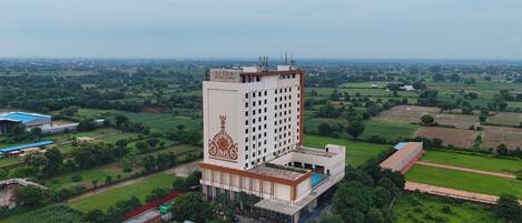 A high-rise hotel with a central courtyard, surrounded by green fields and a distant cityscape.