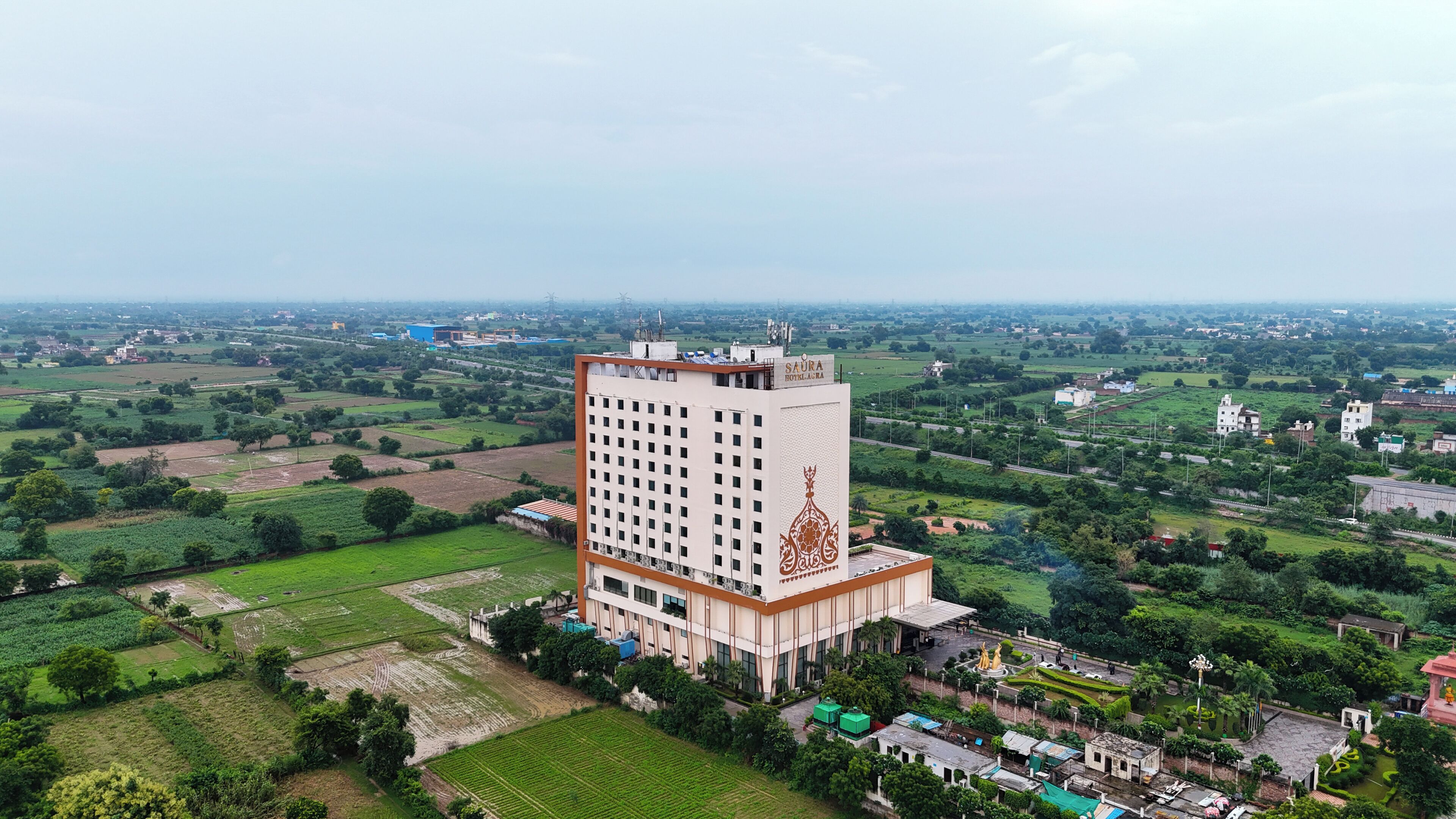 A high-rise hotel with a central courtyard and a view of surrounding fields.