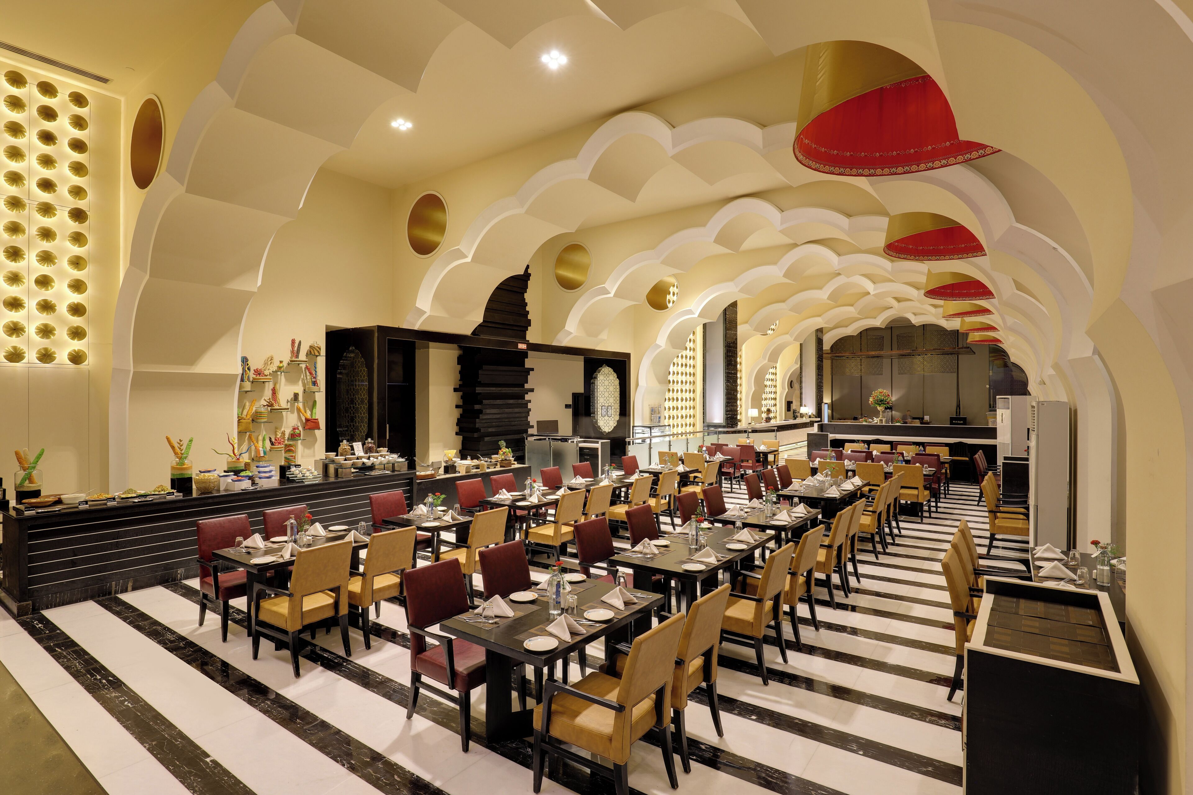 Un restaurante espacioso con varias mesas y sillas, una barra negra y un techo decorativo con arcos y diseños circulares.