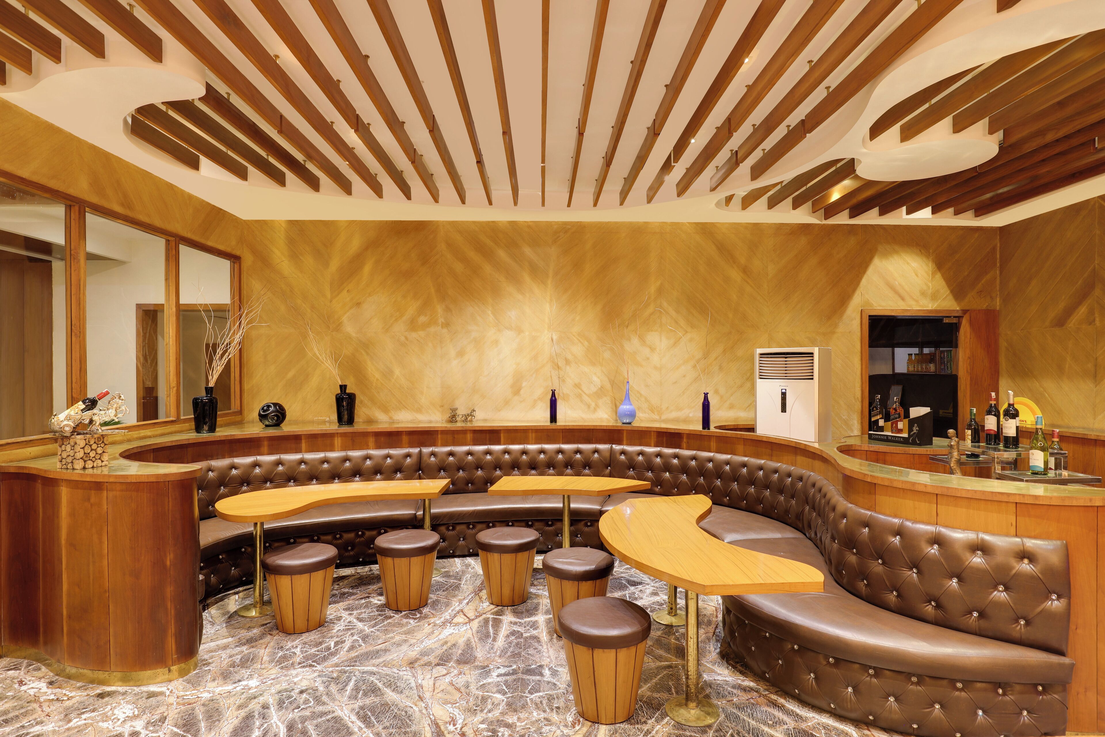 A modern bar area with a curved seating arrangement, wooden ceiling beams, and a marble floor.