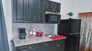 A kitchen with dark cabinets, a microwave, a red slow cooker, a coffee maker, and a black refrigerator. - Charming studio ,minutes from the airport. (Hialeah)
