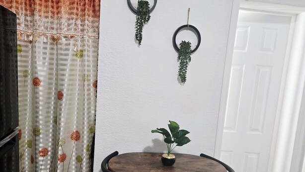 A dining area with a round wooden table and four chairs, a potted plant on the table, and two hanging planters on the wall. - Charming studio ,minutes from the airport. (Hialeah)