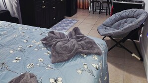A compact room with a bed, a small kitchenette, a dining area, and a grey chair. - Charming studio ,minutes from the airport. (Hialeah)