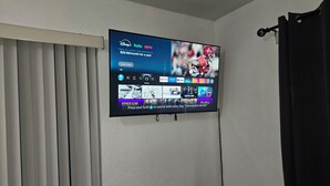 A flat-screen TV mounted on a wall displaying a streaming service interface with various content options. - Charming studio ,minutes from the airport. (Hialeah)