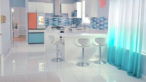 Una cocina moderna con armarios blancos, una isla central con taburetes y un respuesto de azulejos azules.