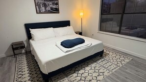 A bedroom with a bed, a ceiling fan, a nightstand, a lamp, a window, and a patterned rug.