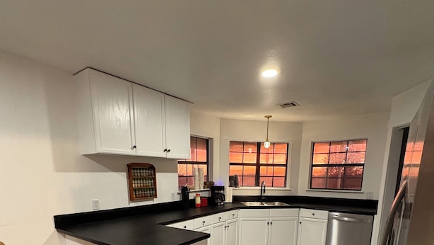 A modern kitchen with white cabinets, a black countertop, and a wooden floor. There are two bar stools and a built-in island.
