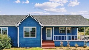 A single-story blue house with a front porch, a small front yard, and a clear sky.