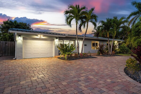 A residential house with a garage, paved driveway, and palm trees.