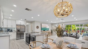 Cocina moderna con armarios blancos, electrodomésticos de acero inoxidable y un comedor con mesa de madera para cuatro.