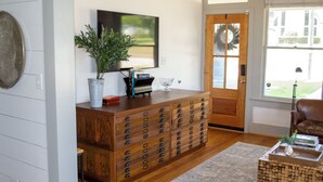 A living room with a wooden dresser, a television, and a door with a wreath. - Immaculately restored home in Downtown Brenham (Brenham)
