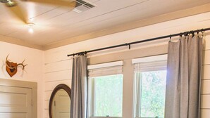A bedroom with a bed, a window with curtains, a mirror, and a wooden floor. - Immaculately restored home in Downtown Brenham (Brenham)