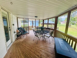 Eine überdachte Veranda mit Holzterrasse, einem Glastisch mit Stühlen und einem Grill.