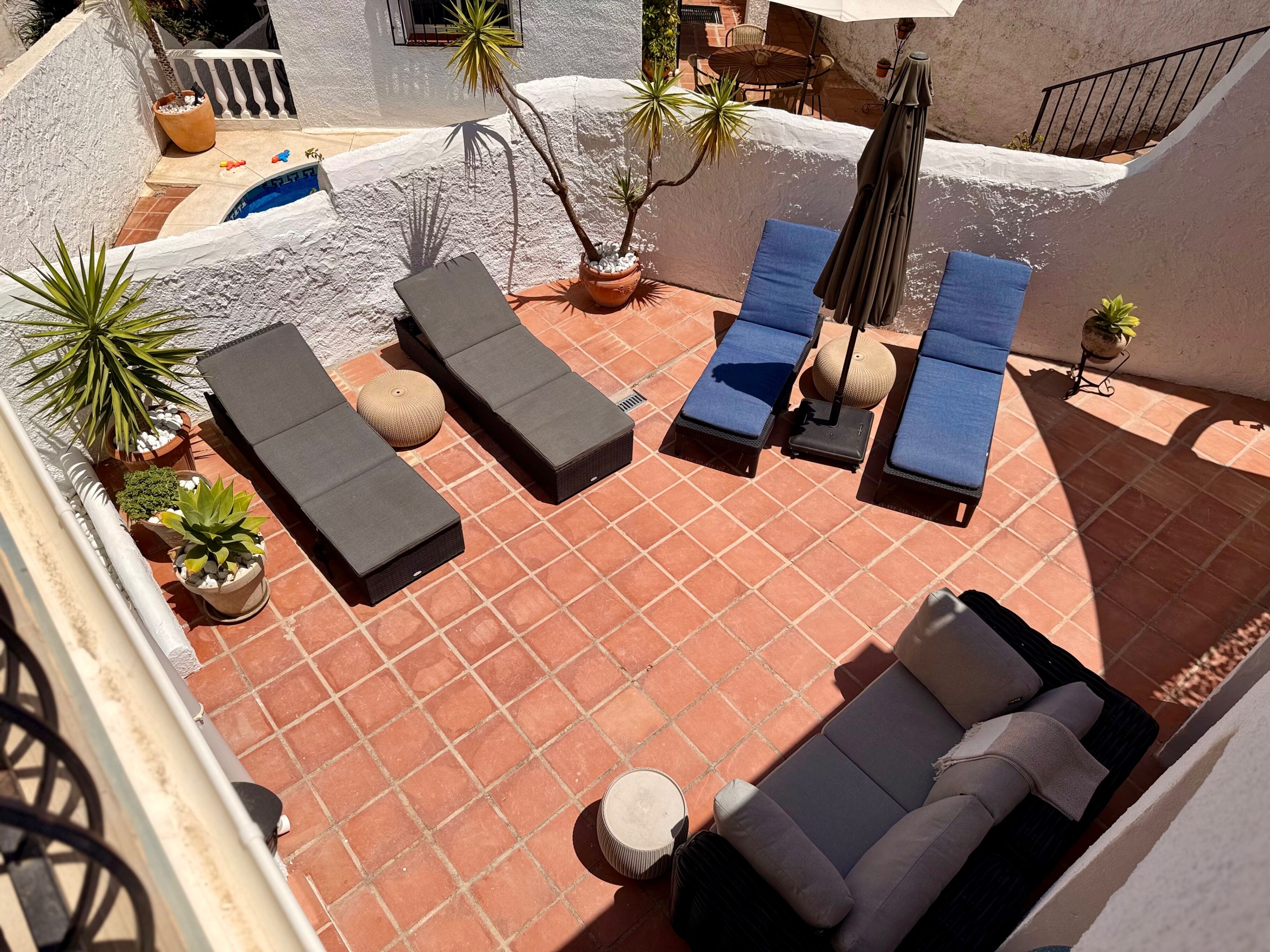 A rooftop patio with sun loungers, a small table, and potted plants.
