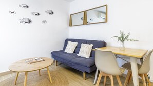 Une pièce avec un canapé bleu, une table à manger en bois, une table basse ronde et un miroir au mur.