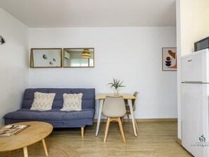 Un espacio de sala con un sofá, una mesa de comedor con sillas, una mesita redonda pequeña, un refrigerador y espejos montados en la pared.