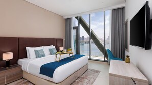 Una habitación de hotel moderna con una cama grande, un escritorio, un televisor y vistas a un horizonte urbano.