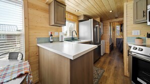 Une cuisine compacte aux murs en bois, dotée d’un îlot central, d’appareils électroménagers en acier inoxydable et d’une fenêtre qui laisse entrer la lumière naturelle.