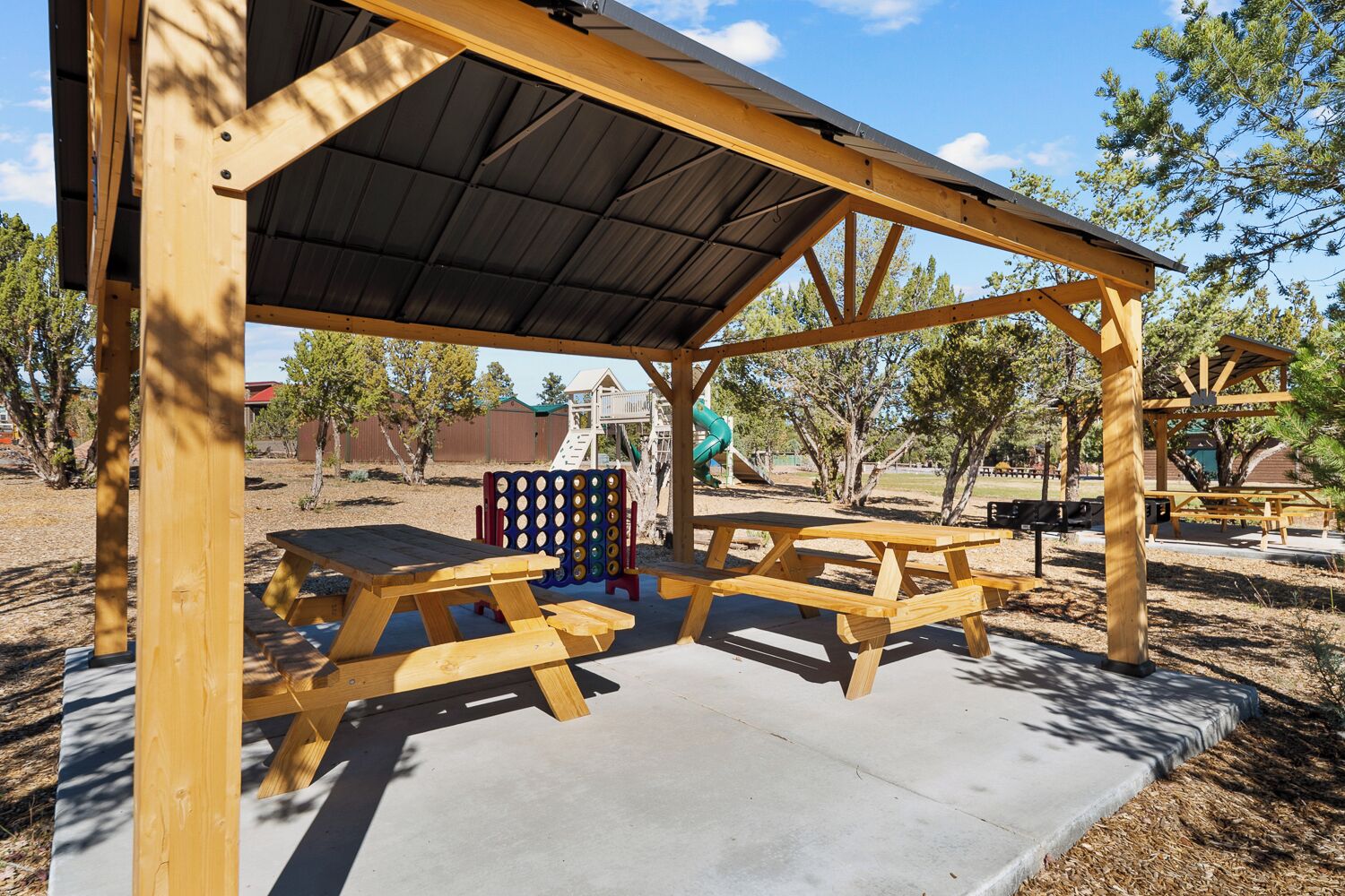 Un pavillon en bois avec des tables de pique-nique et, au fond, une aire de jeux.