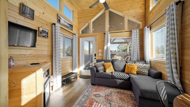 L’intérieur d’un chalet accueillant, avec un canapé, un ventilateur de plafond et une grande fenêtre.