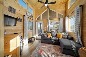 A cozy cabin interior with a sofa, a ceiling fan, and a large window. - The Peaceful Pine Cabin at Rocky Rim Resort (Overgaard)