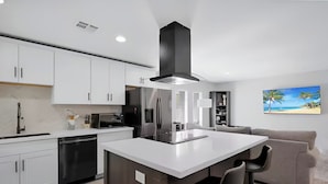 A modern kitchen with white cabinets, a stainless steel refrigerator, and a central island with bar stools.