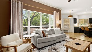 A living room with a grey sofa, a wooden coffee table, and a view of the outdoors through large windows.