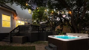 A backyard with a hot tub, wooden deck, and string lights.