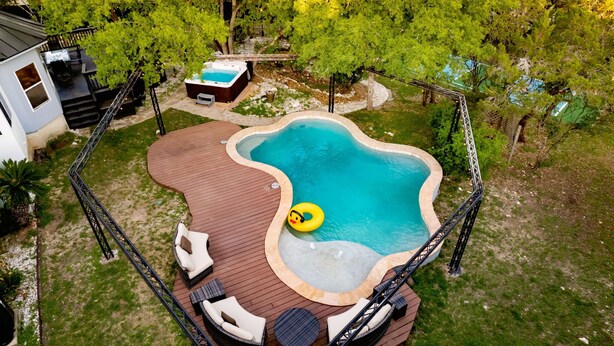 A hot tub surrounded by a wooden deck with lounge chairs and a small pool.