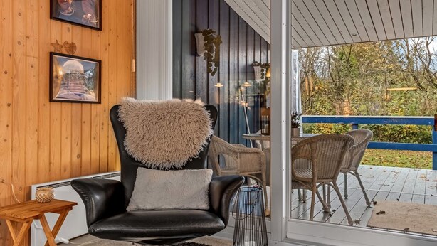 Ein modernes Interieur mit einem schwarzen Ledersessel, einem Holztisch und einer Glastür, die auf eine Terrasse im Freien führt.