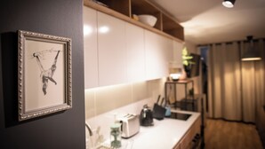 Une cuisine avec des meubles blancs, un tableau encadré au mur et un plan de travail sur lequel se trouvent une bouilloire et un grille-pain.
