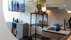 Une cuisine moderne avec un téléviseur à écran plat fixé au mur, une petite table agrémentée d’une plante en pot et un meuble de rangement au-dessus du plan de travail.