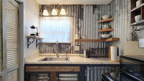 A kitchen with a sink, stove, and shelves with dishes.