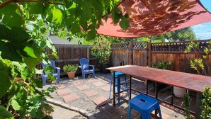A patio area with a wooden table and blue chairs, surrounded by a wooden fence and potted plants.