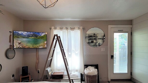 A bedroom with a bed, a TV, a ladder, a mirror, a basket, and a door with a 'No Smoking' sign.